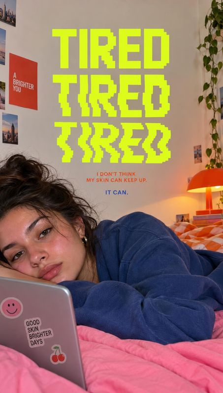 lifestyle scene product photo: A woman in a blue sweatshirt lounges on pink bedding beside a laptop in a cozy bedroom, beneath oversized neon-yellow typography…