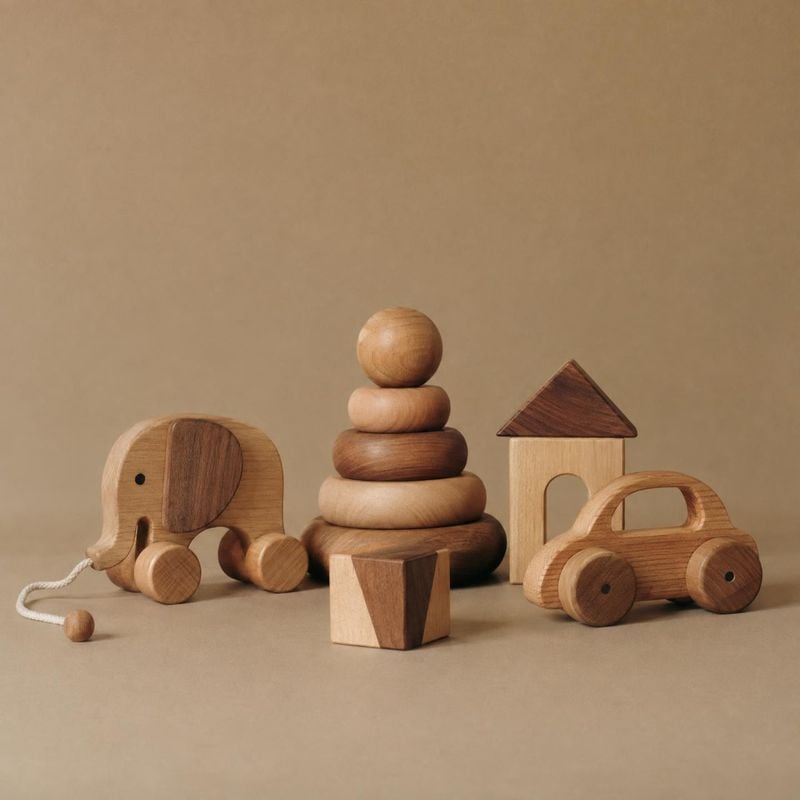 wooden toy set toys product photo: A collection of wooden toys—a pull-along elephant, stacking rings, a small house, and a car—is arranged on a warm beige stud…
