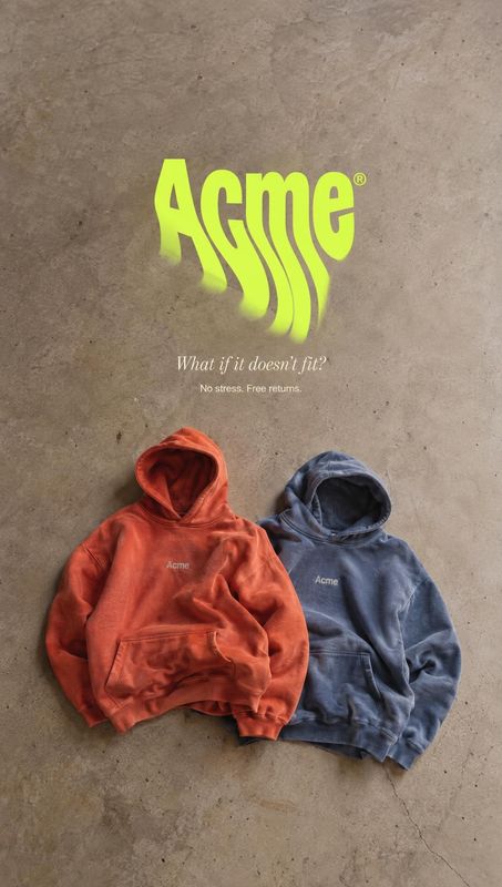 hoodies flat lay product photo: Two rust-red and slate-blue hoodies lie on a textured concrete surface beneath oversized neon-green lettering and a small retur…