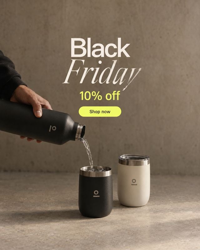 insulated bottle and tumblers splash / pour product photo: A hand pours water from a black insulated bottle into a matching tumbler beside a cream tumbler, set…