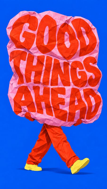 action & motion product photo: A person in vivid red clothing and yellow shoes carries an oversized crumpled pink sign reading “GOOD THINGS AHEAD” against a sa…