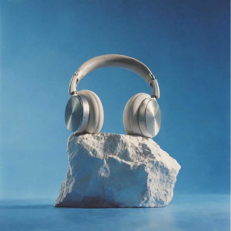wireless headphones electronics product photo: Silver over-ear headphones rest on a rugged white stone against a softly lit blue studio backdrop, creating a co…