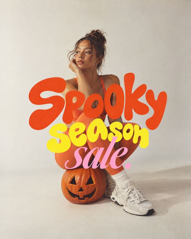 sneakers halloween product photo: A woman in sporty apparel and white sneakers poses beside a carved pumpkin against a pale studio backdrop, with bold orange,…