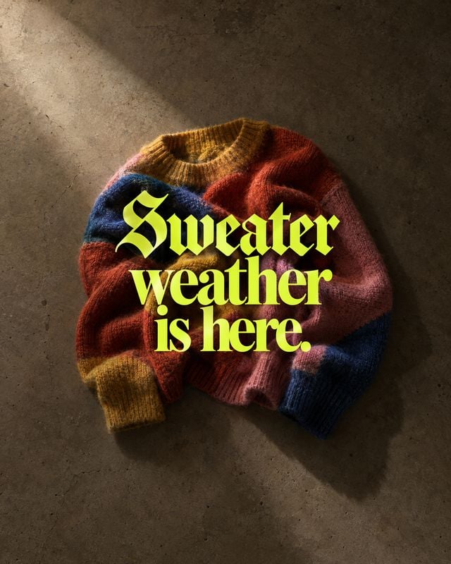 color-block knit sweater autumn product photo: A folded multicolored knit sweater rests on a textured concrete surface under warm directional light, with bold…