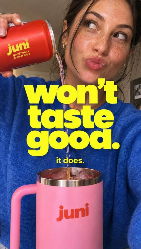Juni canned drink splash / pour product photo: An adult woman in a bright blue sweater pours a red Juni can into a pink mug, with bold yellow headline letterin…