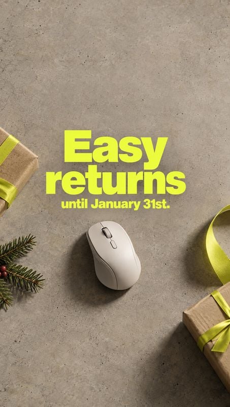 computer mouse electronics product photo: A white computer mouse sits on a textured gray surface among gift boxes, bright ribbon, and evergreen sprigs, beneath…