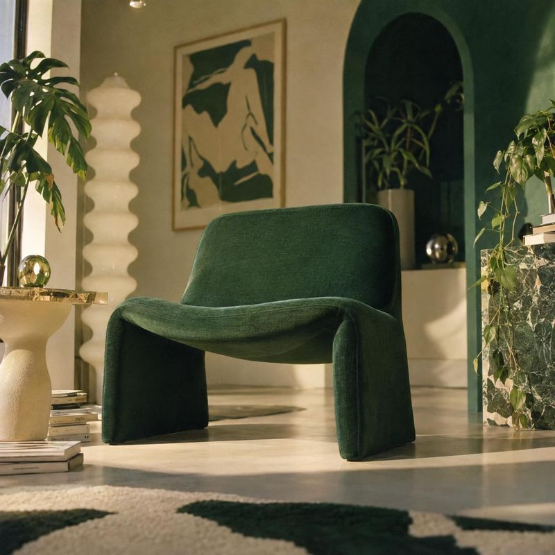 green upholstered lounge chair interior space product photo: A sculptural deep-green lounge chair sits among plants, art, and warm modern furnishings in a soft…