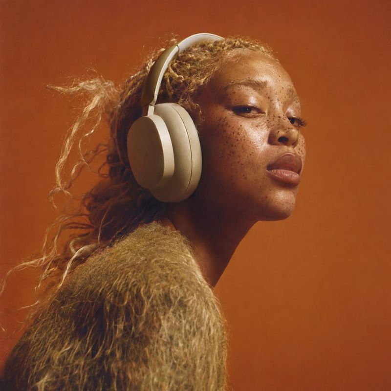 over-ear headphones equipment in use product photo: A model wearing cream over-ear headphones and a textured knit top poses against a warm terracotta studio ba…