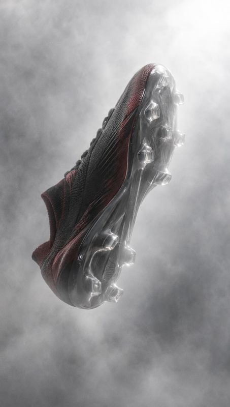 soccer cleat floating product product photo: A dark soccer cleat floats diagonally in a cloud of soft gray smoke, its translucent studded sole catching dramati…