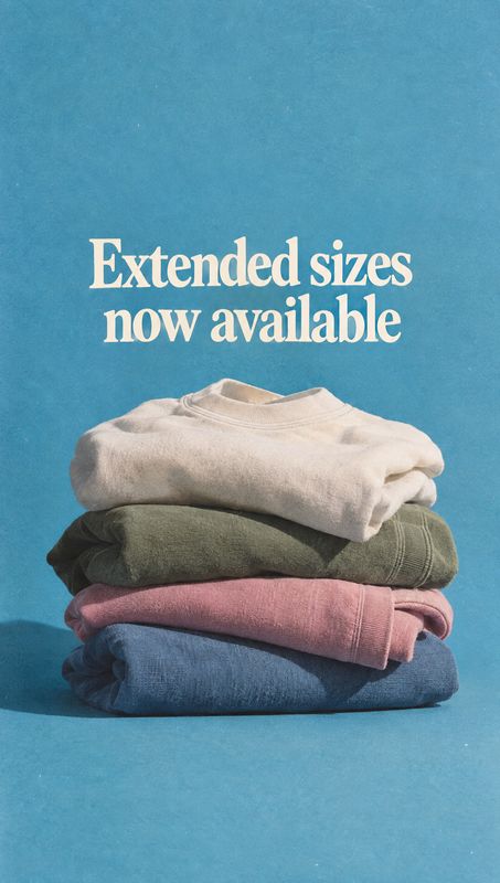 folded sweatshirts fashion product photo: A neatly stacked assortment of folded sweatshirts sits against a bright blue studio backdrop beneath a large cream he…