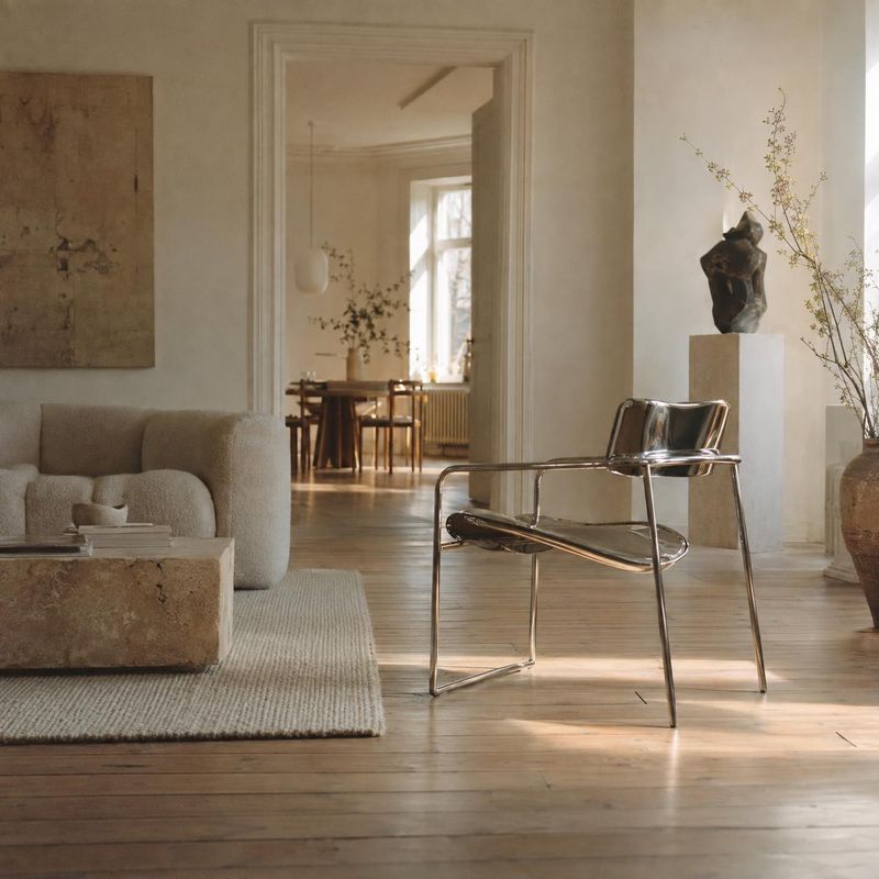 modern lounge chair interior space product photo: A sculptural chrome lounge chair anchors a softly lit living room with neutral upholstery, warm wood floors,…