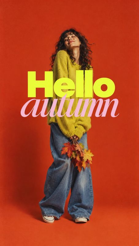sweater and jeans autumn product photo: A curly-haired woman in a mustard knit sweater and loose blue jeans holds autumn leaves against a vivid red studio back…