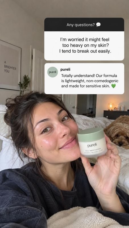 moisturizer product in hand product photo: A woman holds a pale green-lidded moisturizer beside her face in a softly lit bedroom, with a dog resting in the bac…