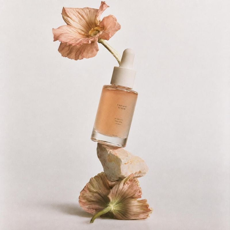 serum bottle floating product product photo: A softly lit serum bottle appears to float between dried blush-toned flowers and a pale stone against a warm, mini…