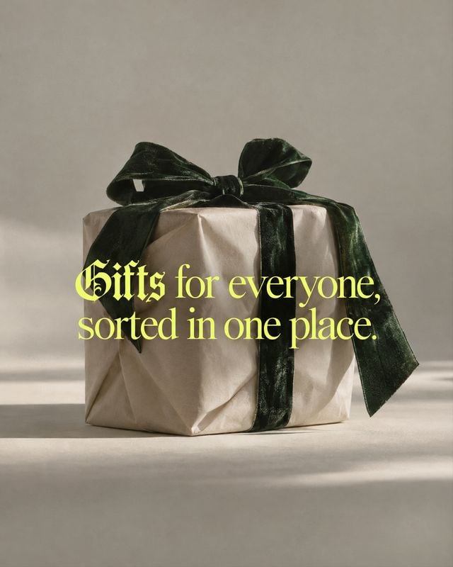 wrapped gift box close-up detail product photo: A neatly wrapped beige gift box tied with a dark green velvet bow sits on a neutral studio surface, with soft d…