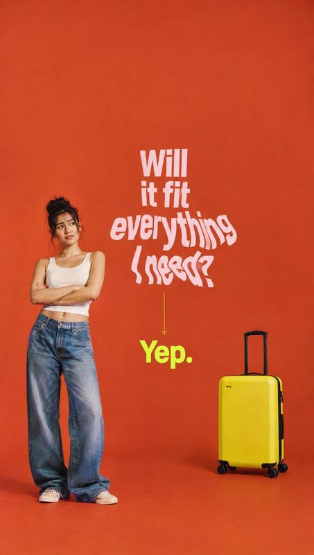 yellow rolling suitcase fashion product photo: A woman in a white tank top and loose blue jeans stands beside a bright yellow rolling suitcase against an orang…