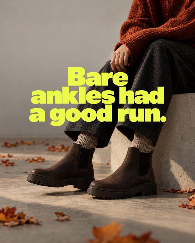 ankle boots autumn product photo: A seated model in a rust knit sweater, dark trousers and brown ankle boots rests against a concrete wall as fallen leaves and…