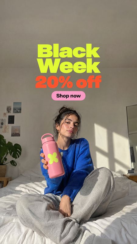 reusable water bottle sports product photo: A woman in a blue sweater sits on a bed in warm window light, holding a pink reusable bottle beneath bold Black Wee…