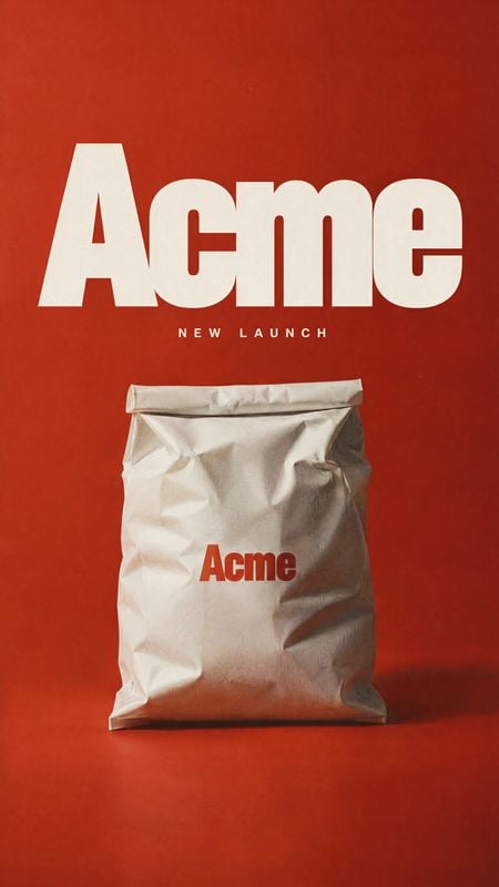 packaged product bag packshot product photo: A crumpled white product bag stands against a vivid red studio backdrop beneath oversized cream “Acme” lettering a…