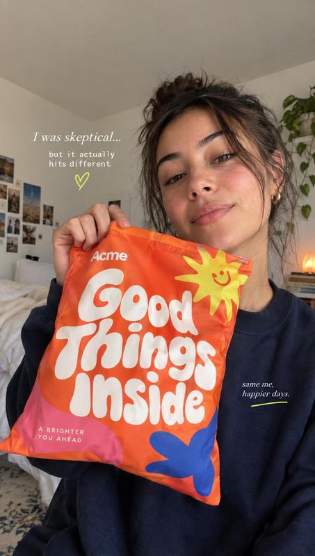 Good Things Inside pouch product in hand product photo: A woman in a dark sweatshirt holds a bright orange pouch toward the camera in a cozy home interior, wit…