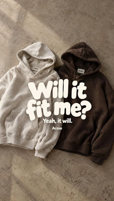 hoodies flat lay product photo: Two hoodies in light and dark neutral tones lie side by side on a textured concrete floor, lit by soft angled light beneath bol…