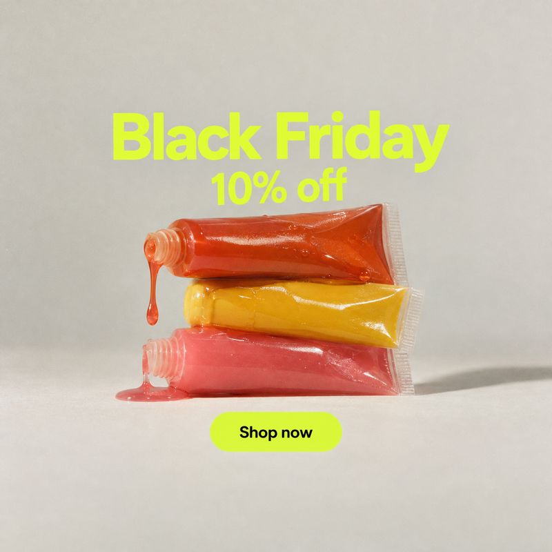 colored cosmetic squeeze tubes texture / swatch product photo: Three glossy red, yellow and pink squeeze tubes are stacked on a pale studio surface beneath neo…