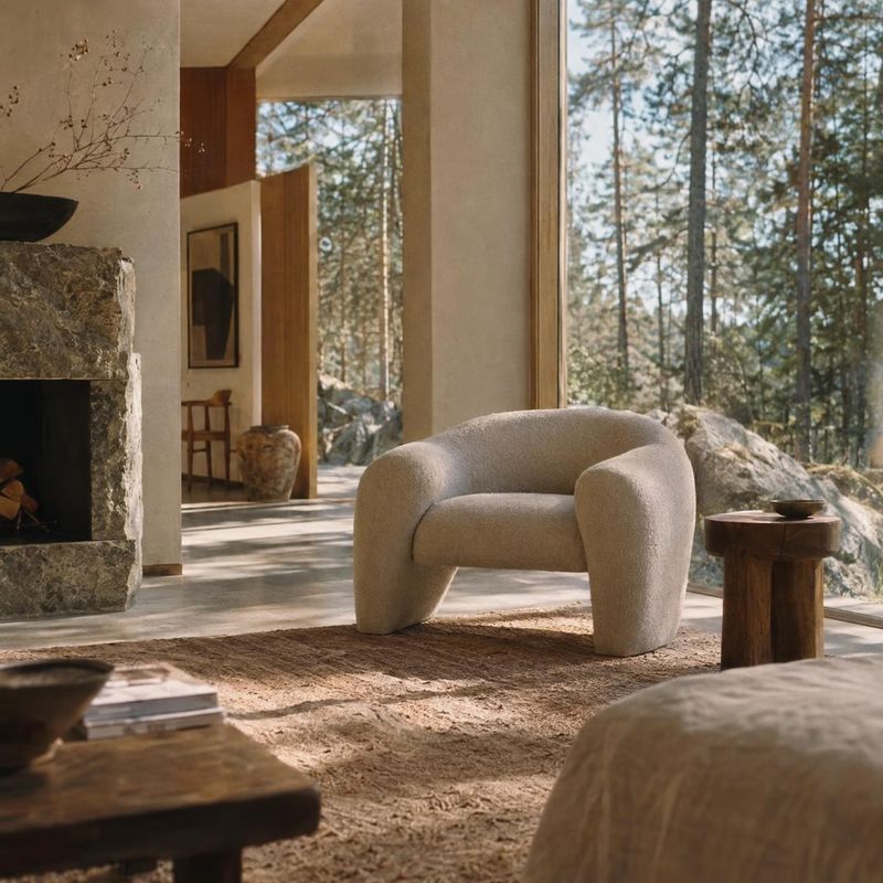 upholstered accent chair interior space product photo: A sculptural cream upholstered chair sits in a warm, natural-material living room, softly lit by sunligh…