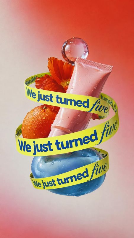skincare products floating product product photo: A pink skincare tube and blue bottle float among an orange, a vivid flower and suspended droplets, wrapped in…
