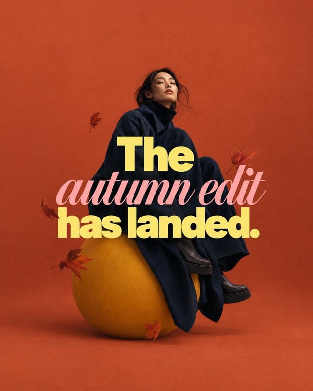autumn outfit with coat and boots autumn product photo: A model in a dark oversized coat and boots poses on a large golden pumpkin against a terracotta studio…