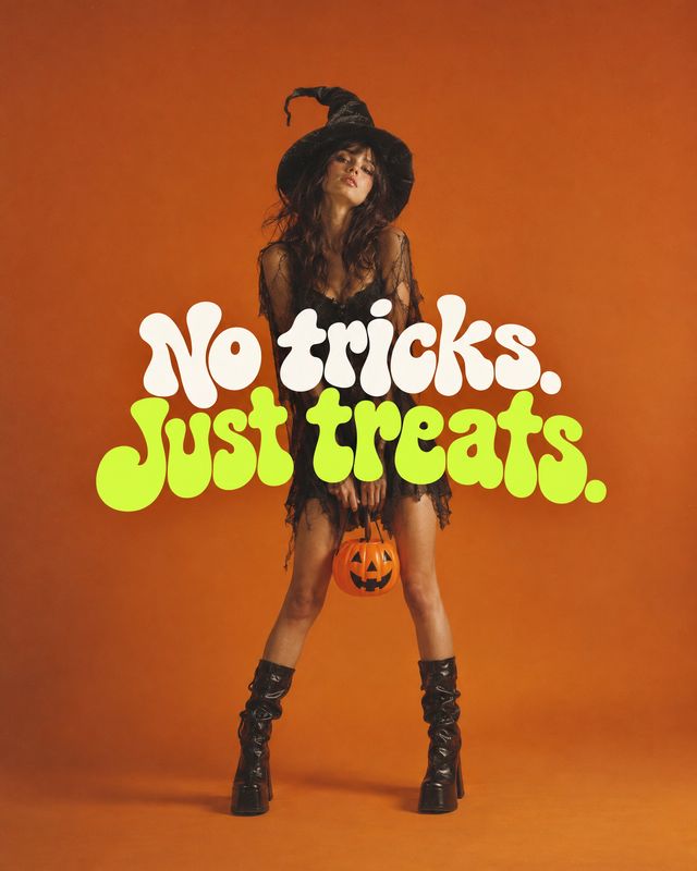 witch costume halloween product photo: A woman in a black witch-inspired outfit and boots poses against a vivid orange studio backdrop, holding a small pumpkin…