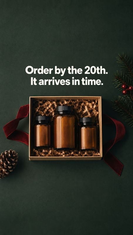 amber bottle gift set personal care product photo: Three amber bottles sit nestled in a gift box with dark red ribbon, pine branches and a pinecone against a d…
