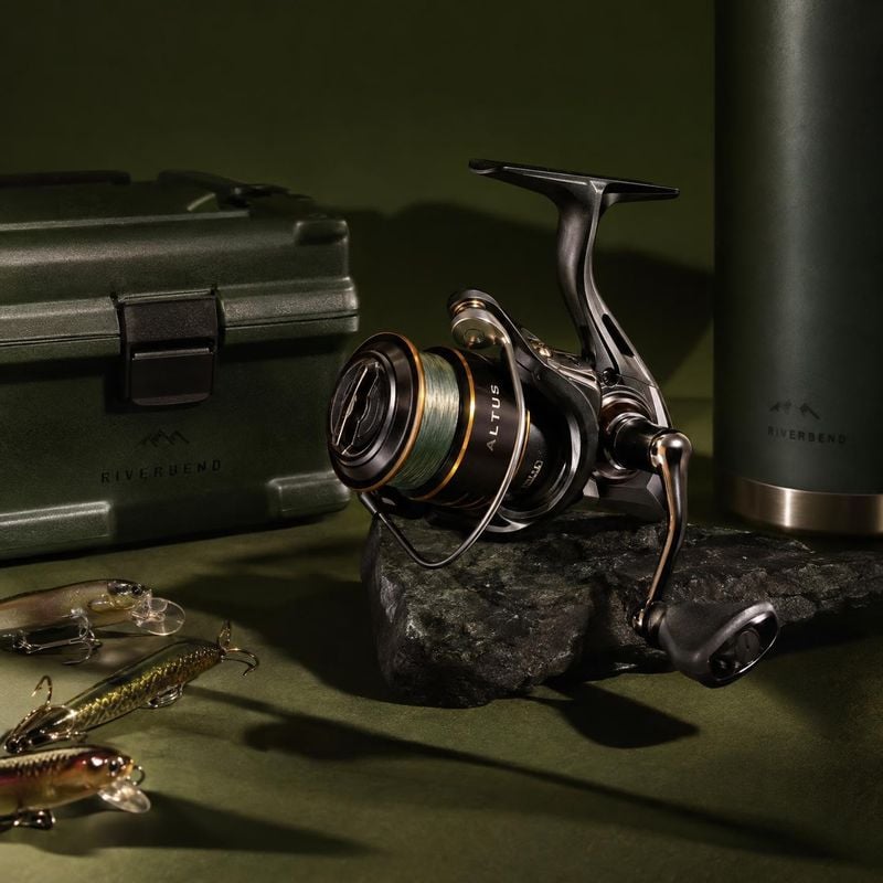 fishing reel and tackle gear sports product photo: A fishing reel, tackle box, bottle and lures are arranged on a dark green set with a textured rock, dramatic…