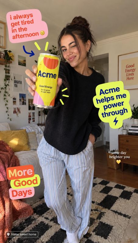energy drink product in hand product photo: A smiling woman in a black sweater and striped trousers presents a colorful energy drink can in a cozy bedroom, wit…