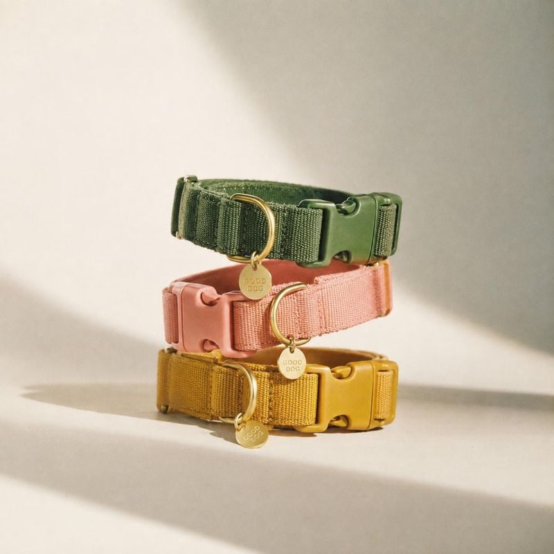 dog collars pet product photo: Three woven dog collars in green, pink, and mustard are stacked against a warm neutral studio backdrop, with soft directional li…