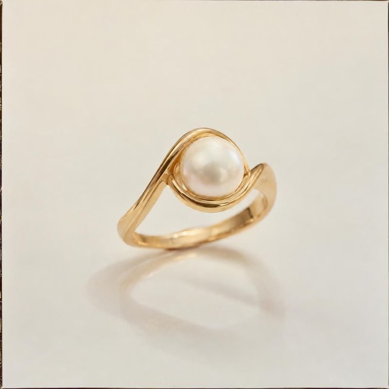 pearl ring jewelry product photo: A gold-tone ring with a luminous pearl is photographed alone against a warm ivory backdrop, with soft lighting and ample open…