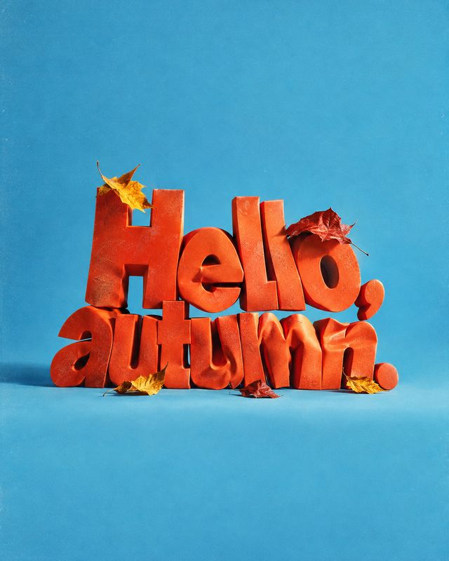 autumn product photo: Bold orange three-dimensional “Hello autumn” lettering sits among fallen leaves against a bright blue studio backdrop, creating a playful…