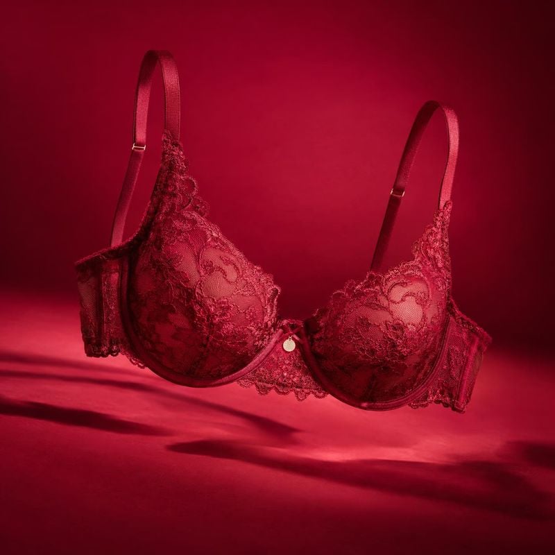 lace bra floating product product photo: A red lace bra floats against a rich crimson studio backdrop, lit with dramatic warm highlights and soft shadows for a…