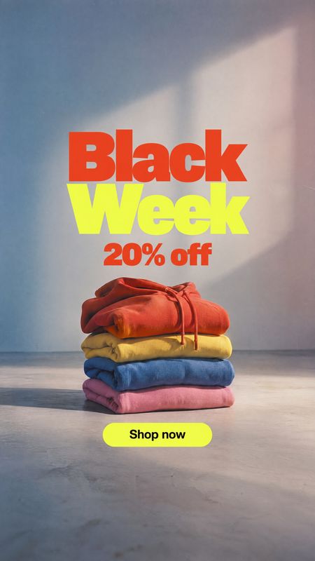 folded clothing fashion product photo: A colorful stack of folded garments sits on a studio floor beneath bold red and yellow Black Week sale typography, with…