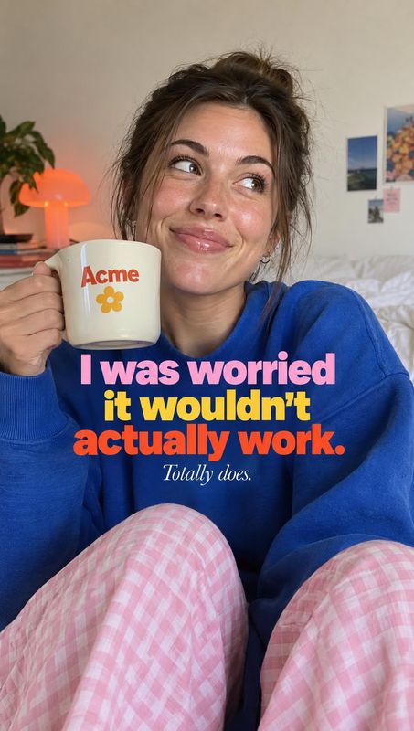 ceramic mug product in hand product photo: A woman in a bright blue sweater and pink checkered trousers holds a branded mug in a cozy bedroom, with warm lamp l…