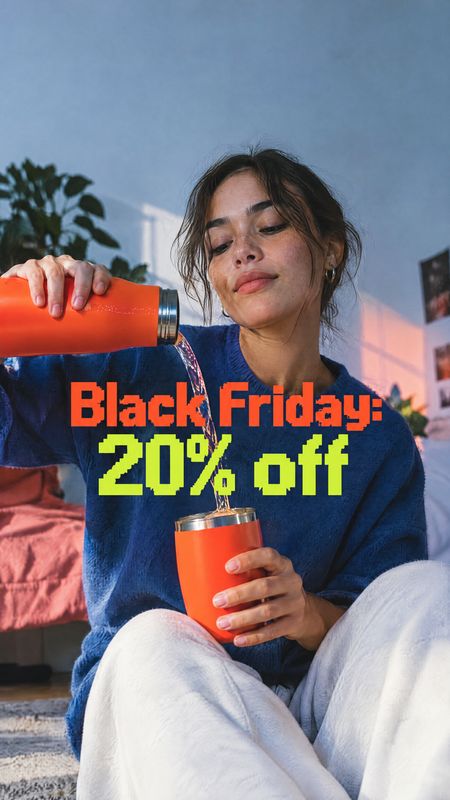 insulated tumbler splash / pour product photo: A woman in a blue sweater pours a drink from an orange insulated tumbler into a matching cup in a cozy interior,…