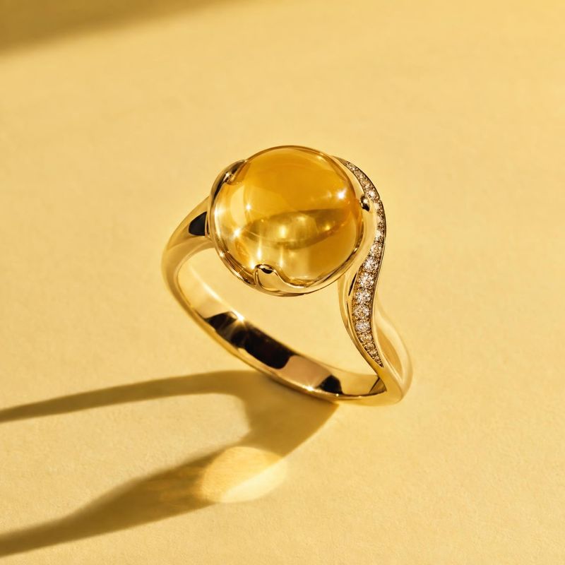 gold ring with amber-colored gemstone close-up detail product photo: A polished gold ring with a large amber-colored stone and a line of small clear stones res…