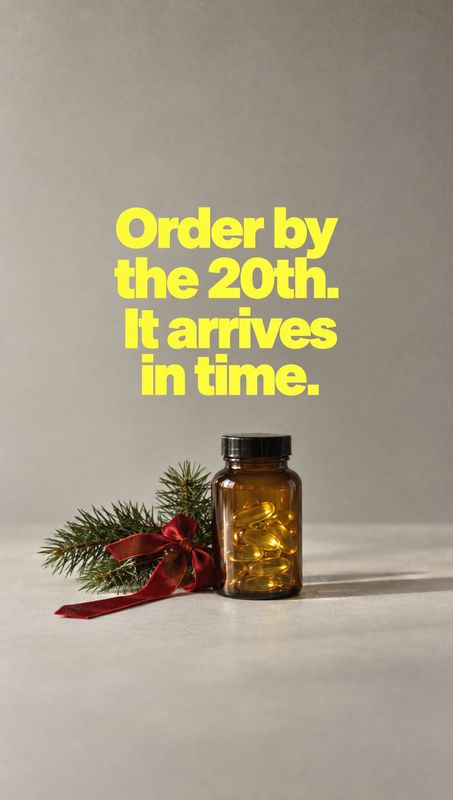 supplement bottle personal care product photo: An amber supplement bottle filled with golden capsules sits beside evergreen sprigs and a red ribbon on a pale s…