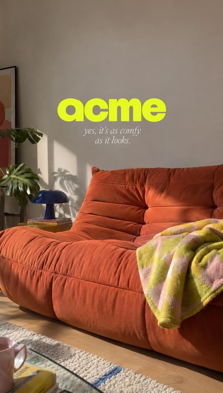 orange sofa room set product photo: A sculptural rust-orange sofa and a soft patterned throw fill a sunlit living room, with plants and a small lamp adding a r…