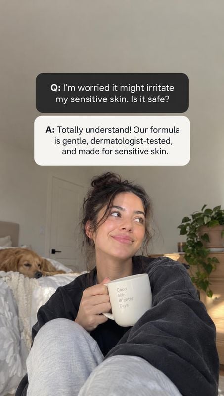 lifestyle scene product photo: A woman in a dark sweatshirt sits on a bed holding a white mug, with a dog and leafy houseplant in the softly lit bedroom and Q&…