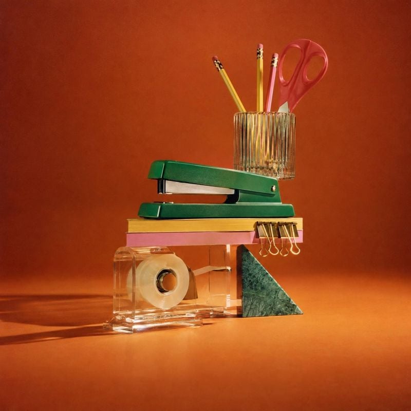 office supplies stationery product photo: A curated arrangement of colorful stationery, including a green stapler, pencils, scissors, clips, and tape, is stage…