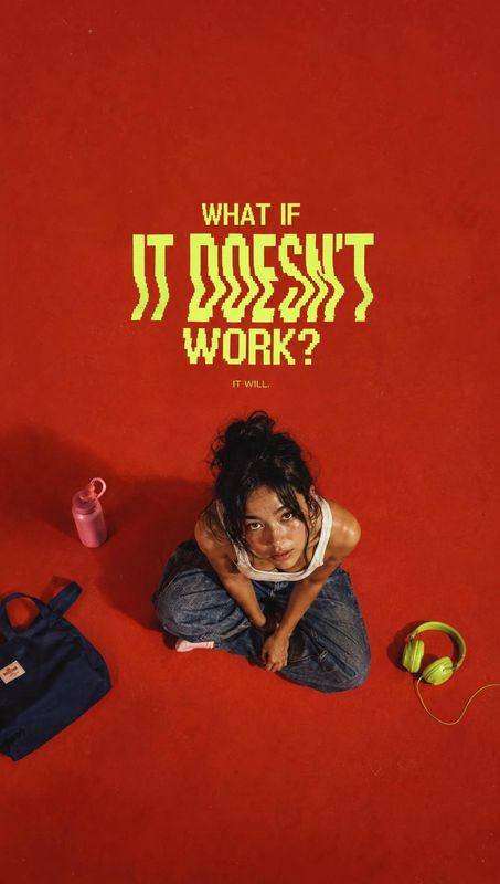 headphones electronics product photo: A young woman looks up from a seated pose on a vivid red studio floor, surrounded by a bag, bottle and headphones beneath…