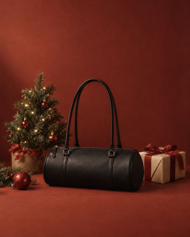 black leather handbag christmas product photo: A structured black handbag sits among a lit Christmas tree and wrapped gifts against a deep red studio backdrop,…