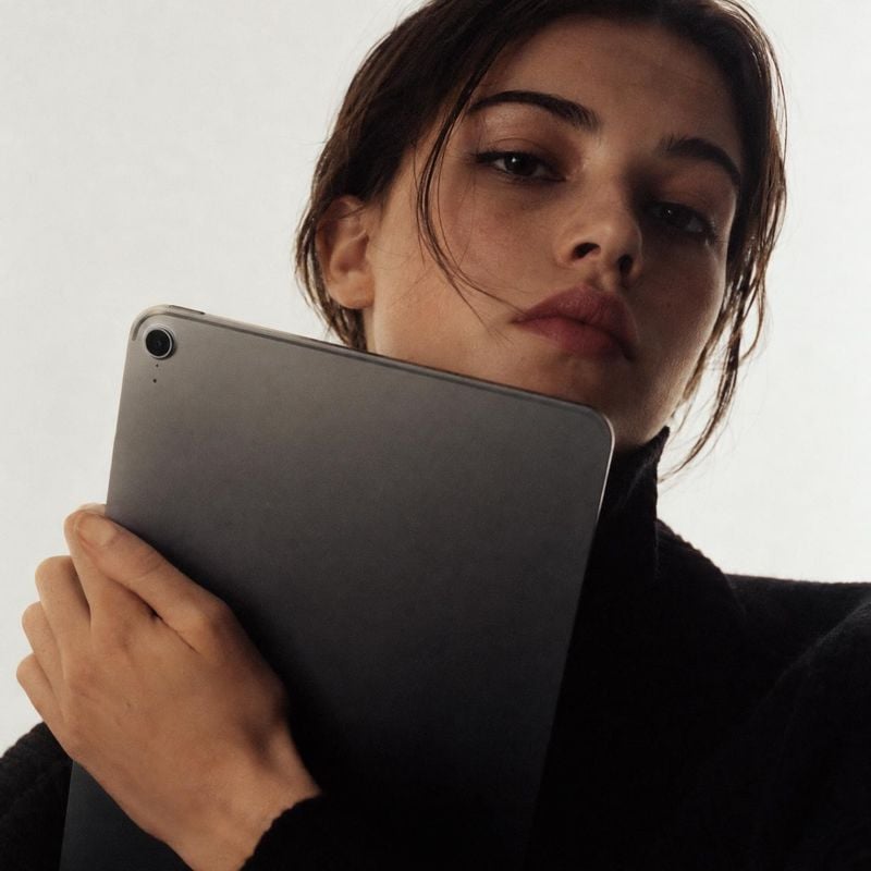 tablet product in hand product photo: A dark-haired woman in a black knit top holds a charcoal tablet close to her face against a softly lit pale background, c…