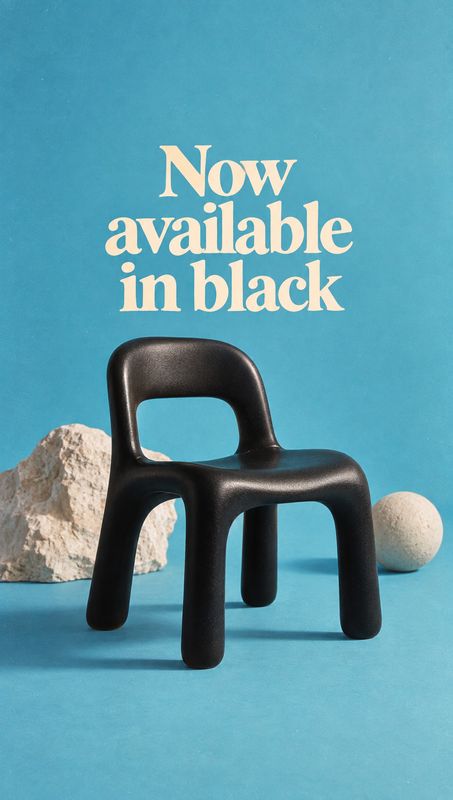 black chair home product photo: A sculptural black chair is staged with pale stone props against a vivid turquoise studio backdrop, beneath large cream letteri…