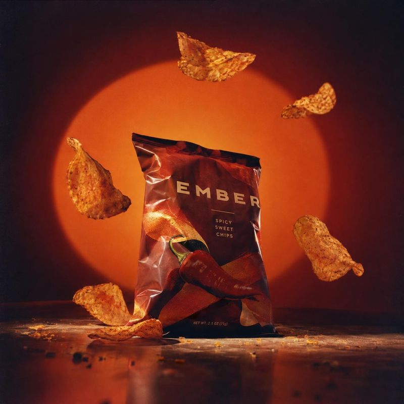 spicy sweet chips food and drink product photo: A bag of spicy-sweet chips stands amid suspended chips against a glowing orange backdrop, with dramatic warm li…